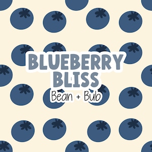 Peut inclure: Un autocollant avec le texte "BLUEBERRY BLISS" et "Bean + Bub" dans une police fantaisiste. Le motif présente des myrtilles bleu foncé sur un fond crème.