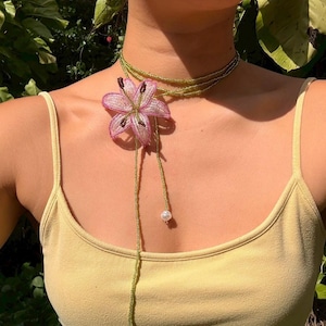Puede incluir: Un collar tipo lariat de cuentas con una hebra larga y fina de cuentas de semillas color verde oliva. El collar incluye una flor de lirio dimensional grande hecha de cuentas rosas y blancas con estambres marrón oscuro y una perla blanca.