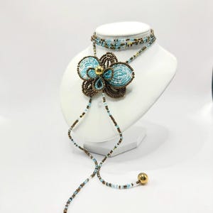 May include: A beaded necklace and choker set displayed on a white mannequin. The necklace features a large, turquoise flower pendant with brown and gold accents. The choker and necklace strands are adorned with small beads in various colors.