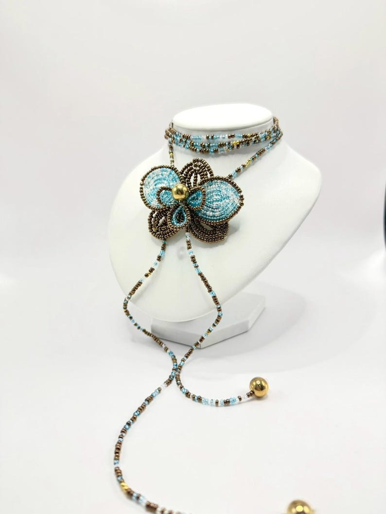 May include: A beaded necklace and choker set displayed on a white mannequin. The necklace features a large, turquoise flower pendant with brown and gold accents. The choker and necklace strands are adorned with small beads in various colors.