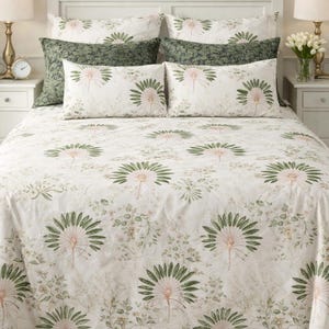 Könnte beinhalten: Ein Bett mit weißem Kopfteil und passenden Nachttischen. Das Bett ist mit einer weißen Bettdecke und Kissenbezügen mit Blumenmuster bedeckt. Das Muster zeigt grüne und rosa botanische Designs. Zusätzliche grün gemusterte Kissen sind ebenfalls vorhanden.