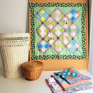 Puede incluir: Una colcha de retazos verde y blanca con un borde floral. La colcha se exhibe en un tablero de corcho con una cesta de mimbre blanca y una cesta de mimbre marrón en primer plano.