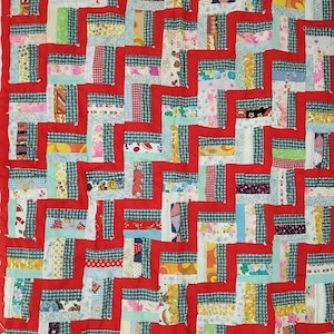 Puede incluir: Una colcha roja de patchwork con un patrón geométrico hecho de varios retazos de tela de colores. La colcha está hecha en un estilo tradicional con un diseño sencillo.
