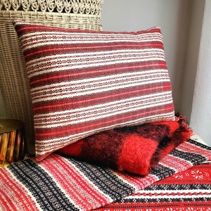May include: A red and white striped throw pillow with a red and black striped throw blanket underneath. The pillow and blanket are made of woven fabric.