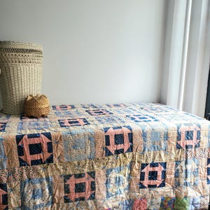 May include: A patchwork quilt with a blue, pink, and white pattern. The quilt is made of squares and is laid out on a bed.