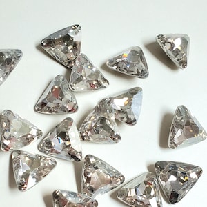 Puede incluir: Una colección de piedras de cristal triangulares transparentes. Las piedras de cristal son facetadas y tienen una superficie brillante y reflectante.
