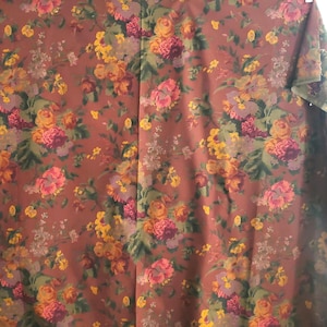 May include: A floral fabric featuring a repeating pattern of roses and other flowers in shades of pink, yellow, and purple against a brown background. The fabric has a vintage or antique aesthetic.