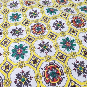 Könnte beinhalten: Nahaufnahme eines weißen Stoffes mit einem sich wiederholenden Muster aus gelben Achtecken und floralen Designs. Die floralen Designs umfassen rote, grüne und gelbe Blumen sowie braune Blätter. Der Stoff hat eine Vintage-Ästhetik.