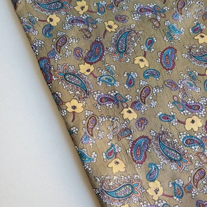 May include: A green fabric with a paisley pattern in shades of blue, purple, orange, and yellow. The fabric has a subtle sheen and a soft texture.