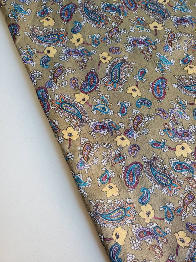 May include: A green fabric with a paisley pattern in shades of blue, purple, orange, and yellow. The fabric has a subtle sheen and a soft texture.