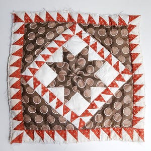 May include: A brown and white patchwork quilt with a red and white border. The quilt is made of squares and triangles, and the pattern is a repeating design.
