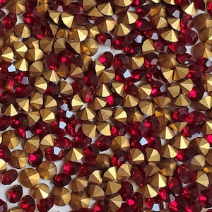 May include: A close-up image of a large quantity of red and gold rhinestones. The rhinestones are scattered randomly and appear to be in a pile.