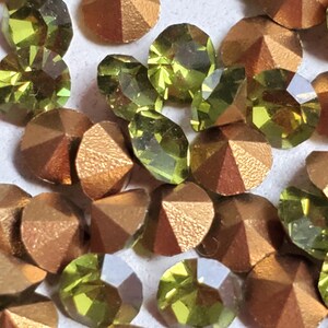 Puede incluir: Surtido de piedras de cristal verdes y doradas. Las piedras de cristal son facetadas y tienen un acabado brillante.