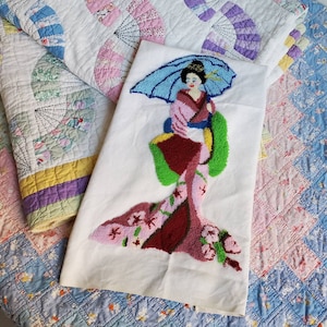 May include: A white fabric panel with a colorful embroidered image of a woman in a traditional Japanese kimono. The woman is holding a fan and has long black hair. The background is a light blue and pink floral pattern.