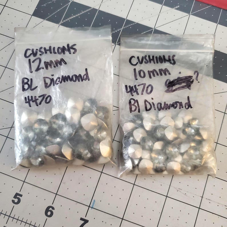 Pu&ograve; includere: Due sacchetti di strass trasparenti, un sacchetto etichettato "CUSHIONS 10mm 4470 BI Diamond" e l'altro etichettato "CUSHIONS 12mm BL Diamond 4470".