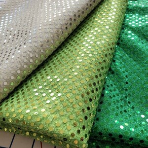 May include: Three rolls of fabric with a sequin pattern. The fabric is silver, light green, and dark green.