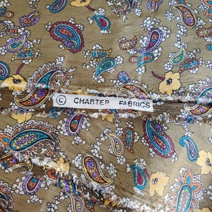 May include: A close-up of a brown fabric with a paisley pattern. The fabric has a white border with the text "Charter Fabrics" printed on it.