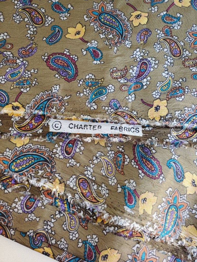 May include: A close-up of a brown fabric with a paisley pattern. The fabric has a white border with the text "Charter Fabrics" printed on it.