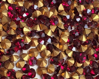 Puede incluir: Primer plano de una colección de gemas facetadas, doradas y rojo rubí. Las gemas están dispersas por la superficie, creando un efecto texturizado y brillante. Las piedras doradas tienen una forma geométrica, similar a una pirámide, mientras que las piedras rojo rubí son más redondeadas.