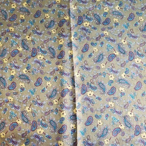 May include: A green fabric with a paisley pattern in shades of blue, yellow, and red. The fabric has a subtle texture and a repeating pattern of paisley shapes and small flowers.