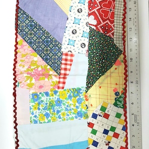 May include: A rectangular patchwork quilt with a red scalloped border. The quilt features various fabric patterns, including floral, gingham, and geometric designs. A ruler is placed next to the quilt for scale.
