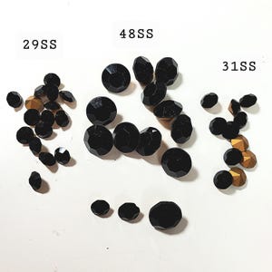 May include: A collection of black, faceted beads of varying sizes, with some gold-coloured beads interspersed. The image features text labels: "29SS", "48SS", and "31SS". The beads are displayed on a white background.
