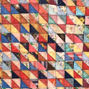 Op de afbeelding: Een patchworkdeken gemaakt van kleurrijke driehoeken van stof. De deken is gemaakt van verschillende stoffen, waaronder bloemenprints, strepen en effen stoffen. De deken is met een eenvoudige steek aan elkaar genaaid.