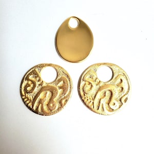 May include: Three gold-colored metal pendants. Two are round with a central hole and an embossed design. The third is an oval shape with a hole at the top. These pendants are suitable for jewelry making.