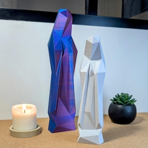 May include: Two geometric sculptures, one in a vibrant iridescent purple and blue, the other in a light gray. Both sculptures are tall and slender, with a modern, abstract design.