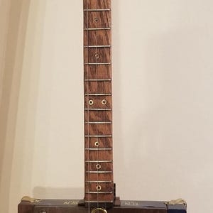 May include: A handmade cigar box guitar with a wooden neck and fretboard. The body is a dark wooden box with blue accents and circular sound holes. The headstock has tuning pegs, and the instrument has strings.