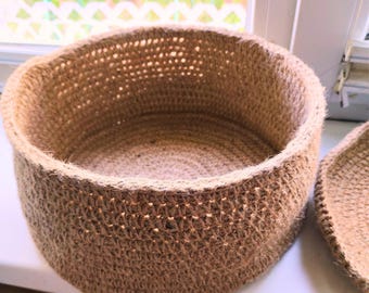 May include: A round, brown, crocheted storage basket with a woven texture. The basket is empty and has a wide opening.