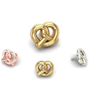 May include: Four pretzel-shaped earrings in different metallic finishes: gold, rose gold, and silver. The earrings are displayed on a white background, showcasing their three-dimensional design and details. The pretzel earrings are a fun and unique accessory.