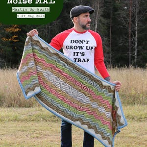 Puede incluir: Una manta estampada multicolor con borde azul es sostenida por una persona que lleva una camiseta roja y blanca con el texto "DON'T GROW UP IT'S TRAP". La manta tiene un diseño en zigzag en varios colores. La imagen también incluye el texto "Beautiful Noise MAL".
