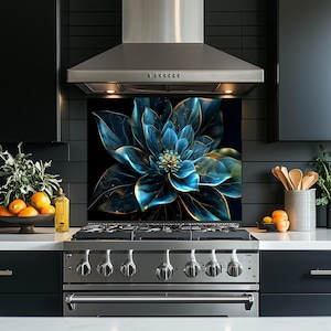 May include: A kitchen backsplash featuring a large, stylized blue flower with gold accents against a black background. The image is centered behind a stainless steel range and hood, with black cabinets and a white countertop.
