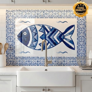 May include: A blue and white fish design on a kitchen backsplash. The fish is painted with geometric patterns and surrounded by a decorative border. The backsplash is above a white farmhouse sink.