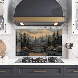 May include: A kitchen backsplash featuring a landscape painting of a forest scene with a bridge over a lake. The painting has a muted color palette with shades of gray, brown, and gold. The backsplash is installed above a gas stovetop.