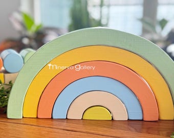 May include: A rainbow-colored wooden stacking toy with seven arches in shades of green, yellow, orange, blue, beige, and yellow. The toy is made of natural wood and is painted with non-toxic paint.  Minerva Gallery is printed on the toy.