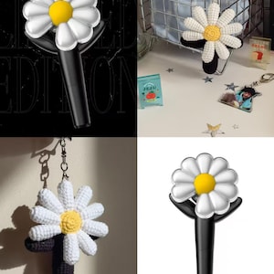 May include: A white crocheted daisy flower keychain with a black stem and a yellow center. The keychain is attached to a silver chain.