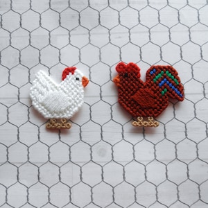May include: Two felt crafts of a rooster and a hen. The rooster is red with a green and blue tail. The hen is white with a red comb. Both are on a white wire mesh background.