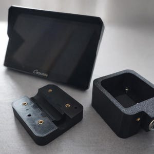 May include: Black electronic device components, including a screen with the word "Carputer" and a key-secured box. The components are arranged on a light grey surface. The screen is rectangular with a black border.