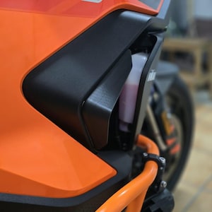 Può includere: Primo piano di una moto arancione e nera. Le parole "SUPER ADVENTURE S" sono visibili sul lato. La moto ha una barra protettiva arancione e un contenitore di liquido trasparente.