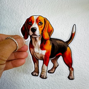 May include: A sticker featuring a Beagle dog illustration. The dog is depicted in a standing pose with a white, brown, black, and orange color scheme. The sticker is held by a hand with a silver ring.