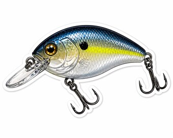 Puede incluir: Adhesivo detallado de un señuelo de pesca. El señuelo tiene una parte superior azul, una sección media amarilla y un cuerpo plateado con un labio de plástico transparente. Cuenta con un anzuelo negro y un ojo dorado.