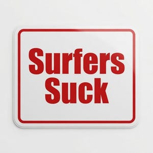 May include: Rectangular white sign with a red border and the words "Surfers Suck" in bold red letters. The sign is centered on a white background.