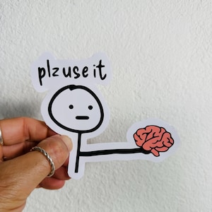 Può includere: Adesivo bianco con un omino stilizzato che tiene in mano un cervello rosa. Il testo "plz use it" è sopra. L'omino ha un'espressione vuota. Sfondo bianco.