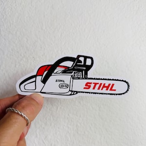 May include: A sticker featuring a stylized chainsaw design. The sticker is primarily white with black and red accents. The brand name "STIHL" is prominently displayed in red on the side and blade of the chainsaw.