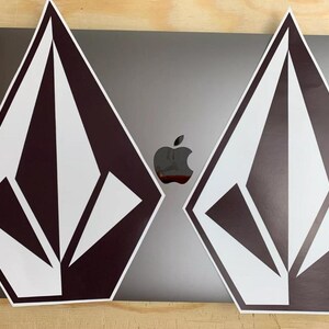 K&ouml;nnte beinhalten: Zwei schwarze und wei&szlig;e rautenf&ouml;rmige Aufkleber mit einem stilisierten Diamantenlogo. Die Aufkleber sind auf einem silbernen Laptop platziert.