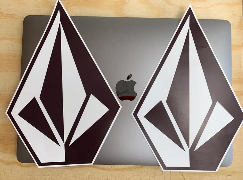 K&ouml;nnte beinhalten: Zwei schwarze und wei&szlig;e rautenf&ouml;rmige Aufkleber mit einem stilisierten Diamantenlogo. Die Aufkleber sind auf einem silbernen Laptop platziert.
