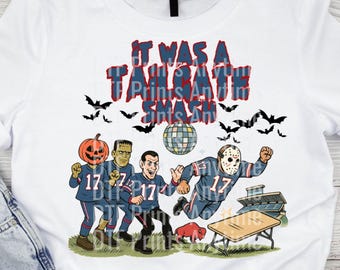 May include: A white t-shirt featuring a graphic of four figures in blue football jerseys with the number 17. The characters include a pumpkin head, Frankenstein, a man, and a hockey-masked figure. Text reads IT WAS A TAILGATE SMASH.