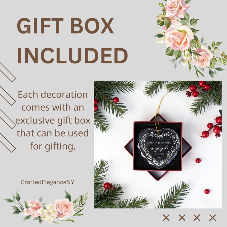 May include: A clear, heart-shaped glass ornament featuring the engraved text "SOPHIA & DANIEL engaged 11.16.2026" surrounded by a leaf wreath. The ornament hangs by a gold string inside a square red gift box, surrounded by pine branches and red berries.